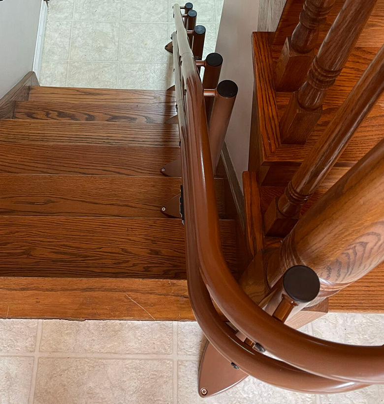 Brown railing for a curved stair lift installation to match brown hardwood floor