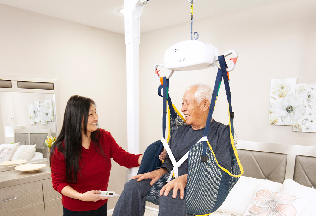 Man in sling using a portable ceiling lift at home with assistance from family