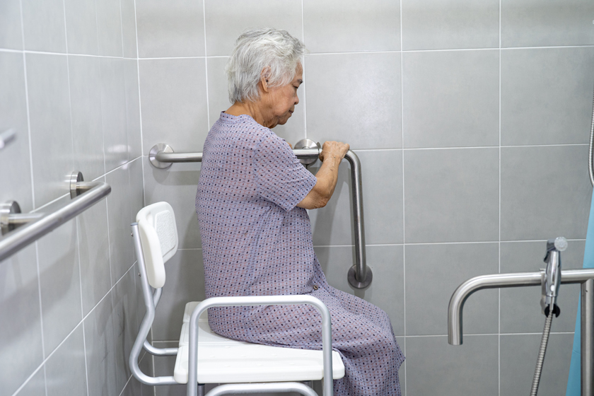 Person in a stationary shower chair holding on to grab bars